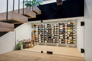 Showcase wine storage with a glass enclosure, wood-finish flooring, and floating wood stairs with black iron railings