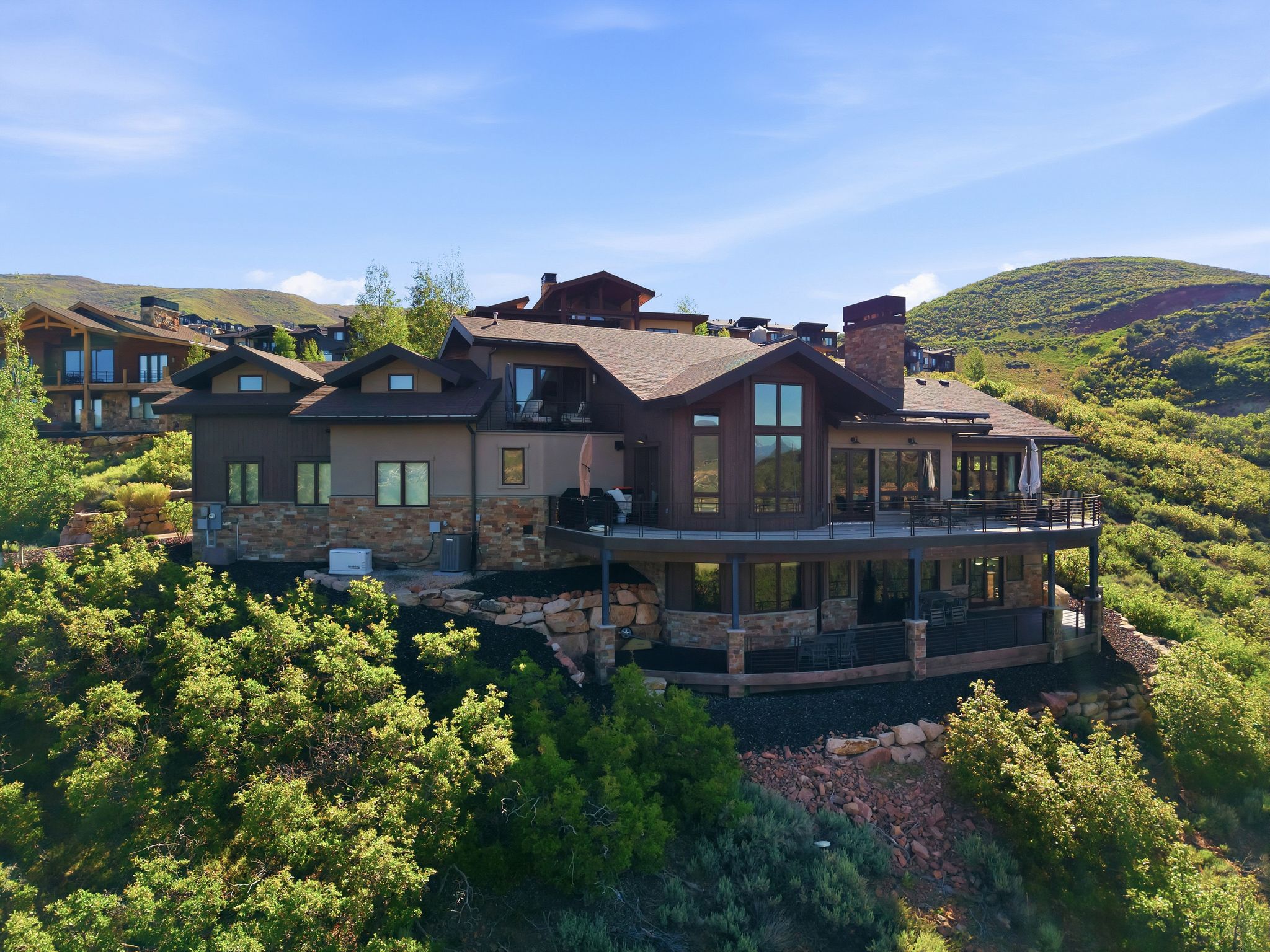 Hillside residence featuring multiple outdoor terraces, integrated stone and wood siding, expansive glass windows, a prominent stone chimney, and a multi-level roofline