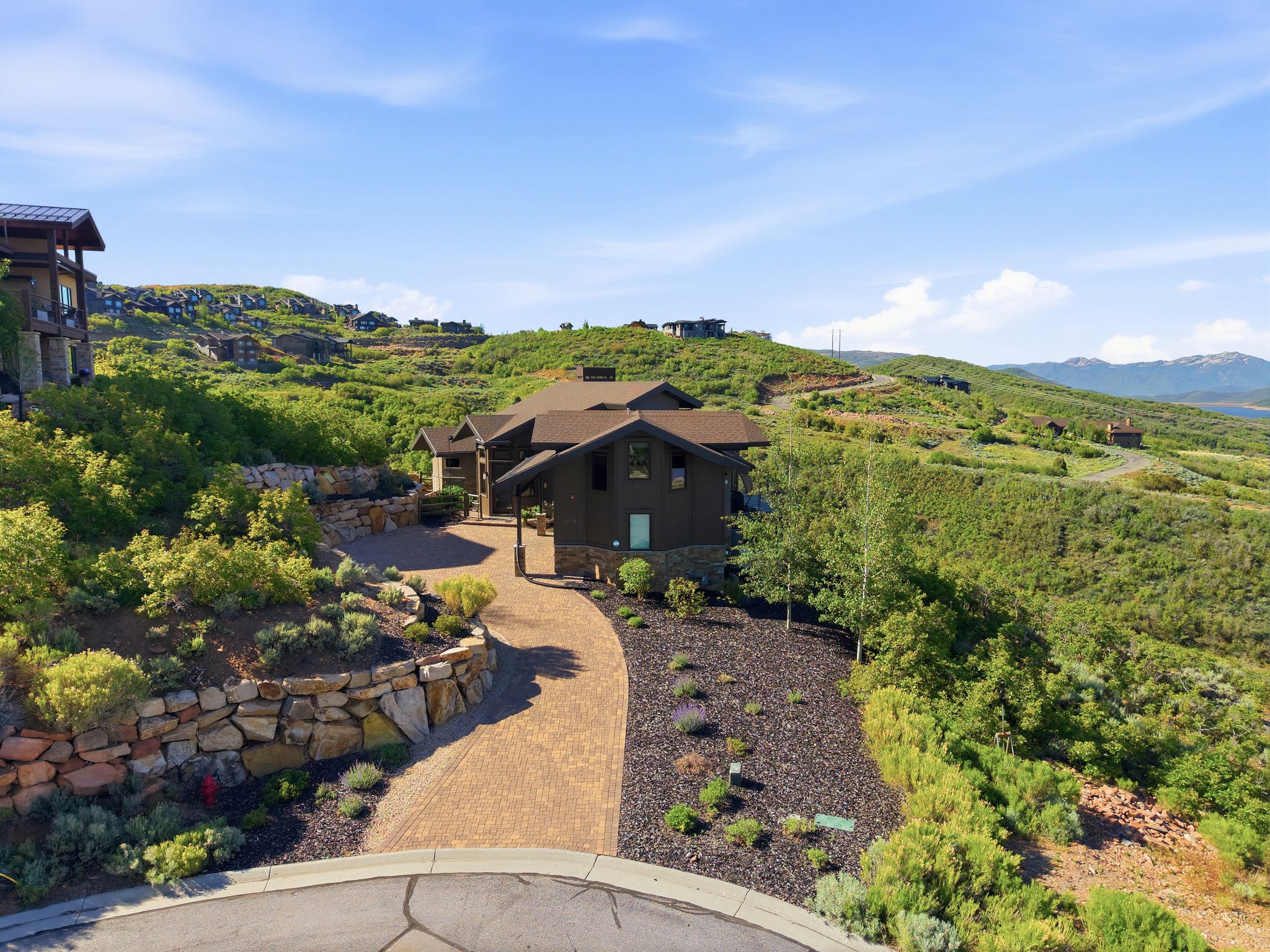 Mountain property featuring a paver driveway, natural stone retaining walls, and extensive landscaping
