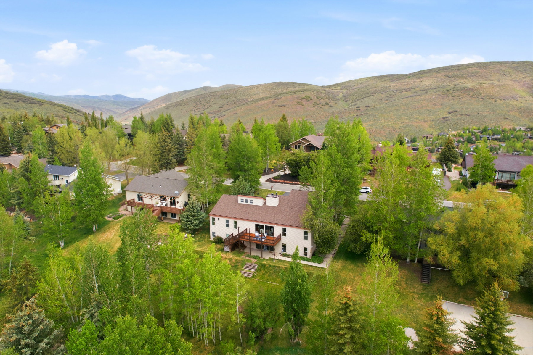 Multi-level home featuring a brown roof and a light-colored exterior, surrounded by mature deciduous and evergreen trees