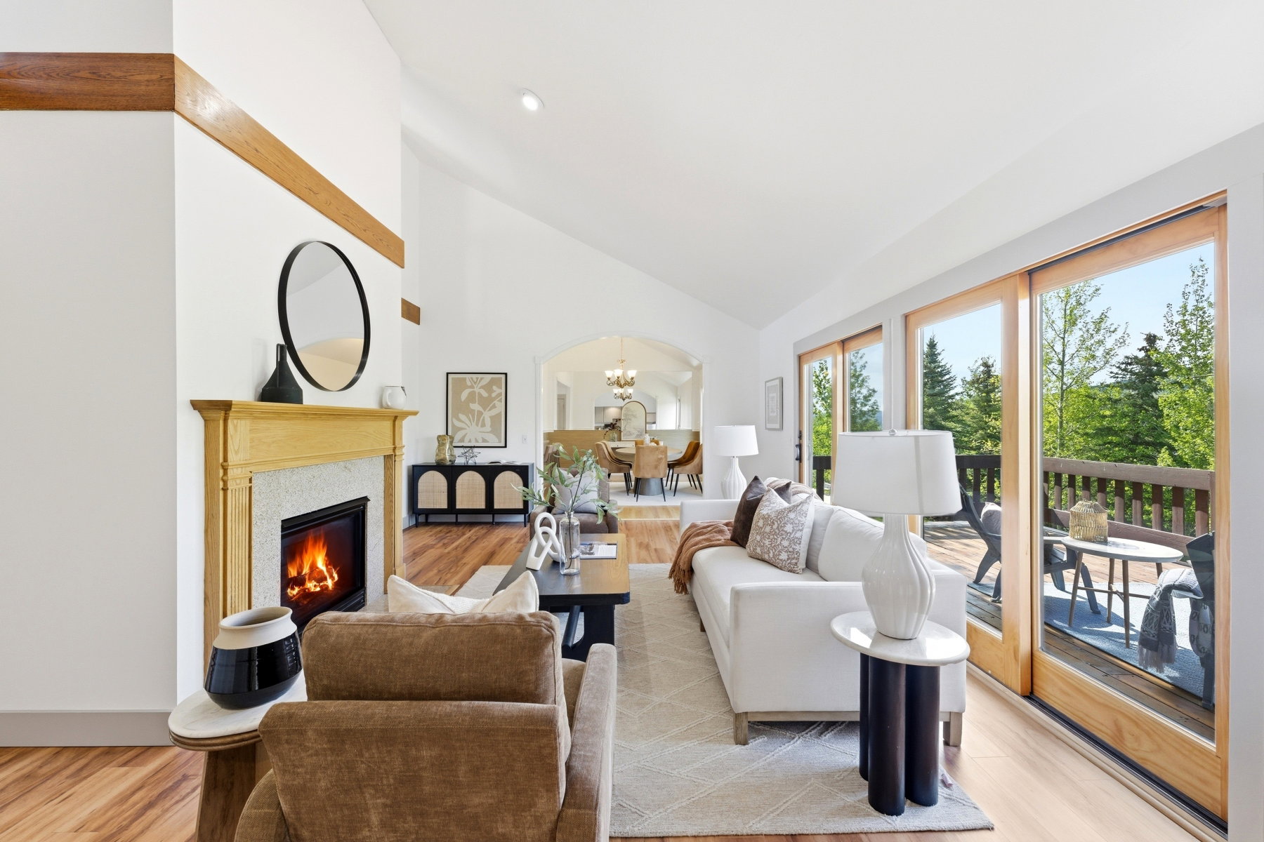 Vaulted ceiling living area featuring a fireplace with a light wood mantel, stone surround, and wood-finish flooring