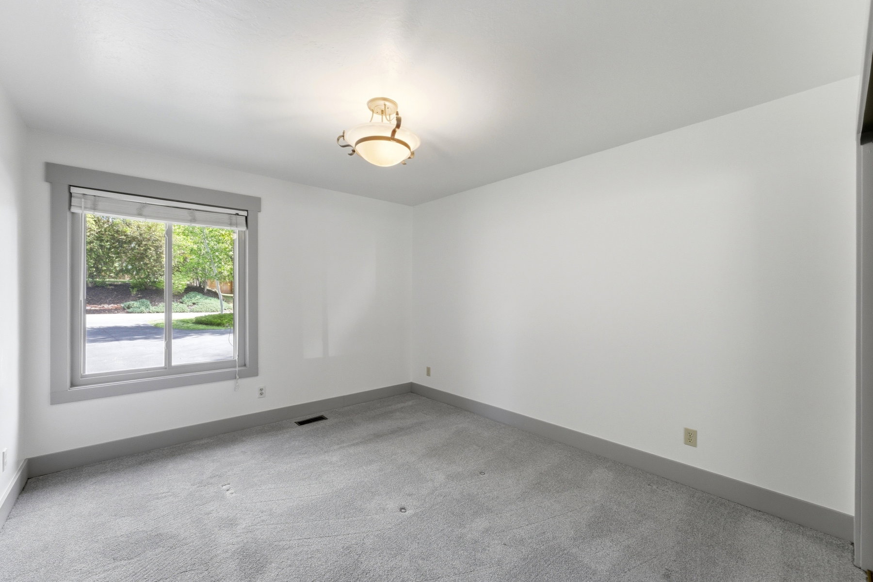 Carpeted room featuring a large window with gray trim, a privacy blind, and a central ceiling light fixture
