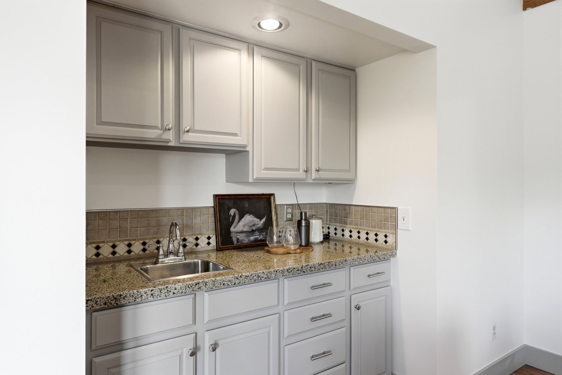 Wet bar featuring shaker-style cabinetry, a stainless steel sink, and a speckled countertop