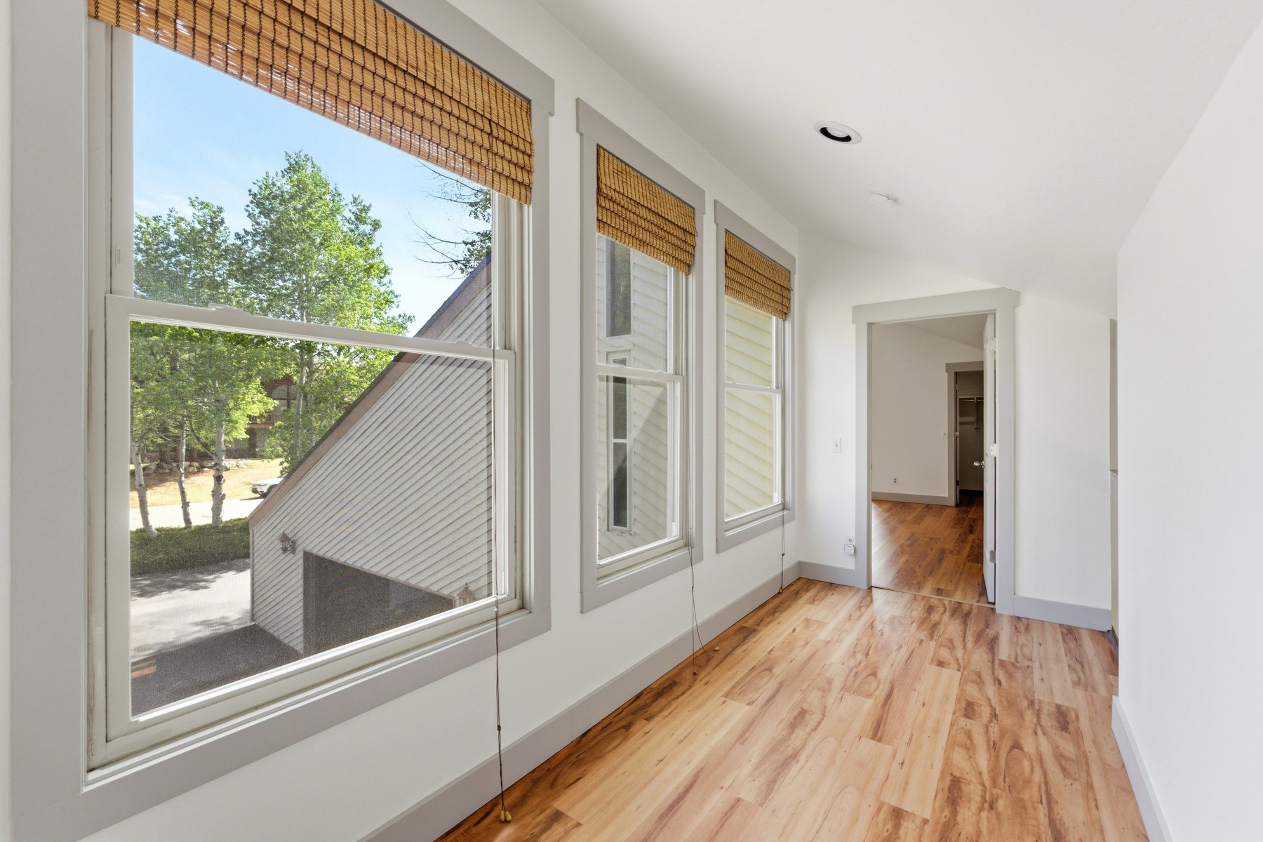 Bright hallway featuring wood-finish flooring, recessed lighting, and multiple windows with woven wood shades