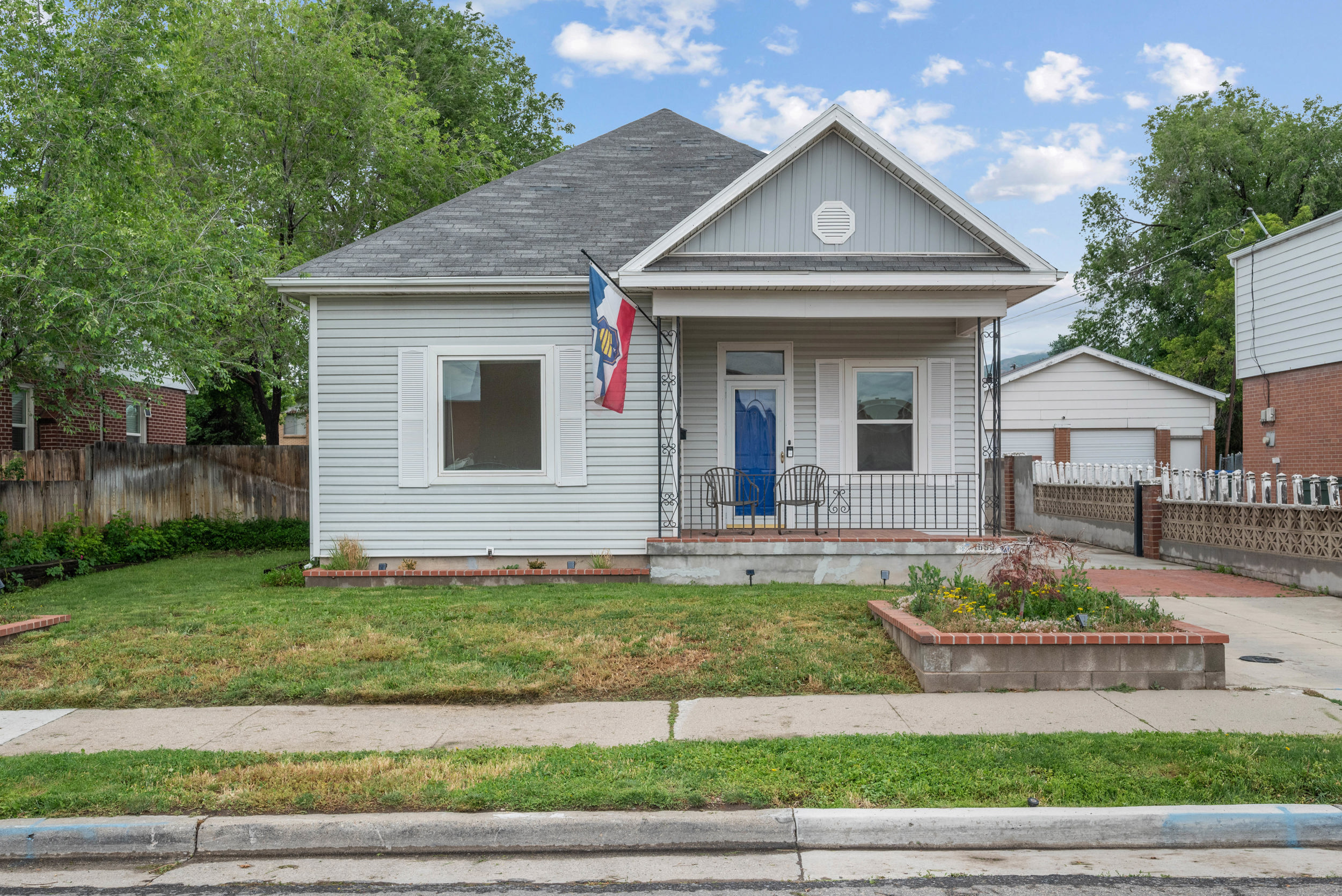 Light gray siding home featuring a covered front porch with wrought iron railings, a prominent gable, and a distinctive blue entry door
