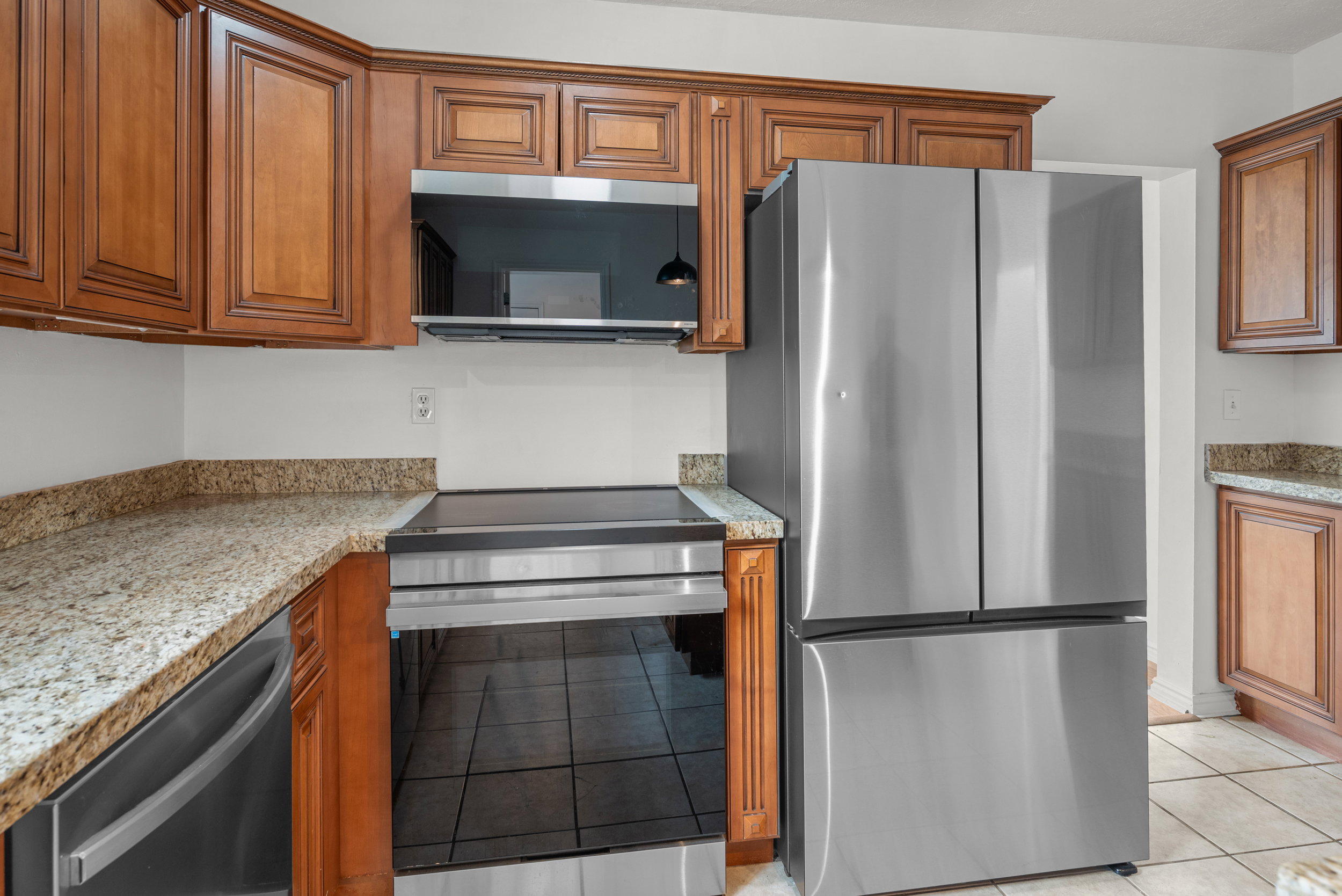 Kitchen featuring wood cabinetry, granite-finish countertops, stainless steel refrigerator, stainless steel range, and tile flooring