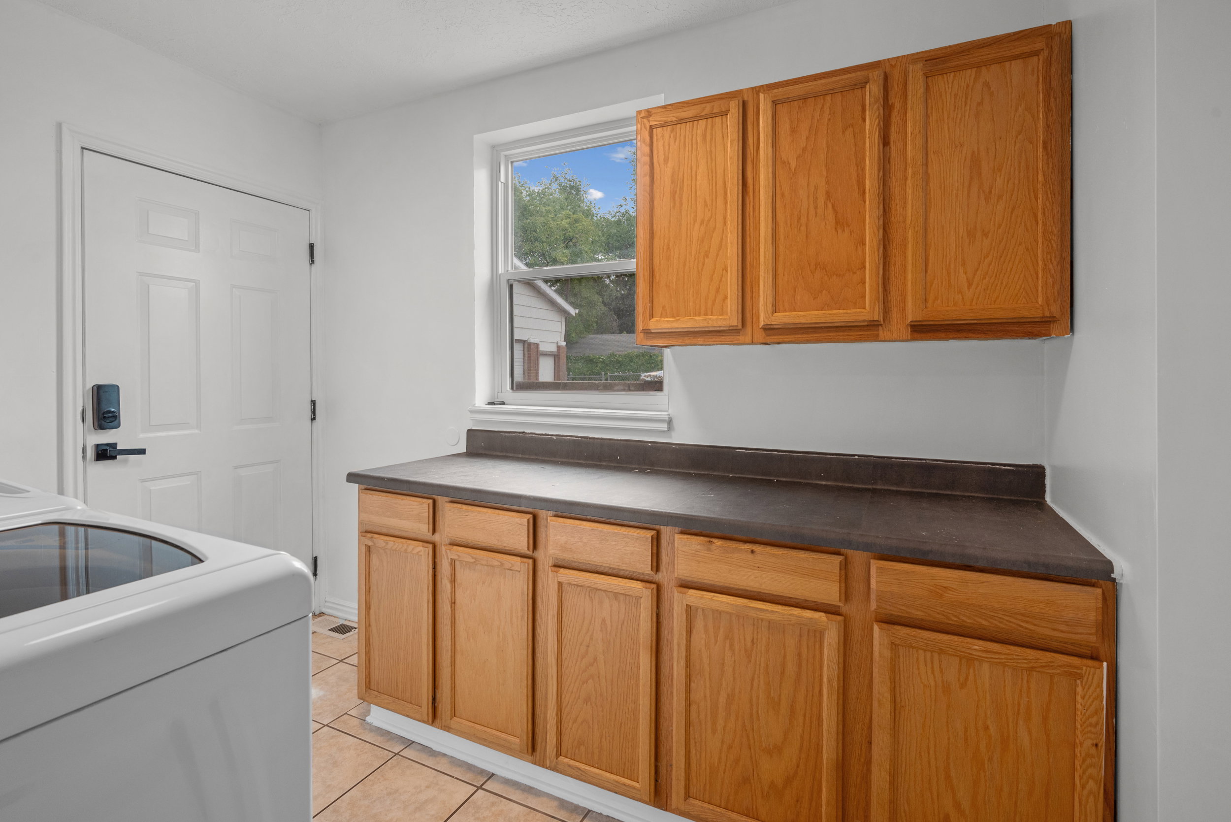 Utility area featuring light wood-finish cabinetry, a dark countertop, and a window providing natural light