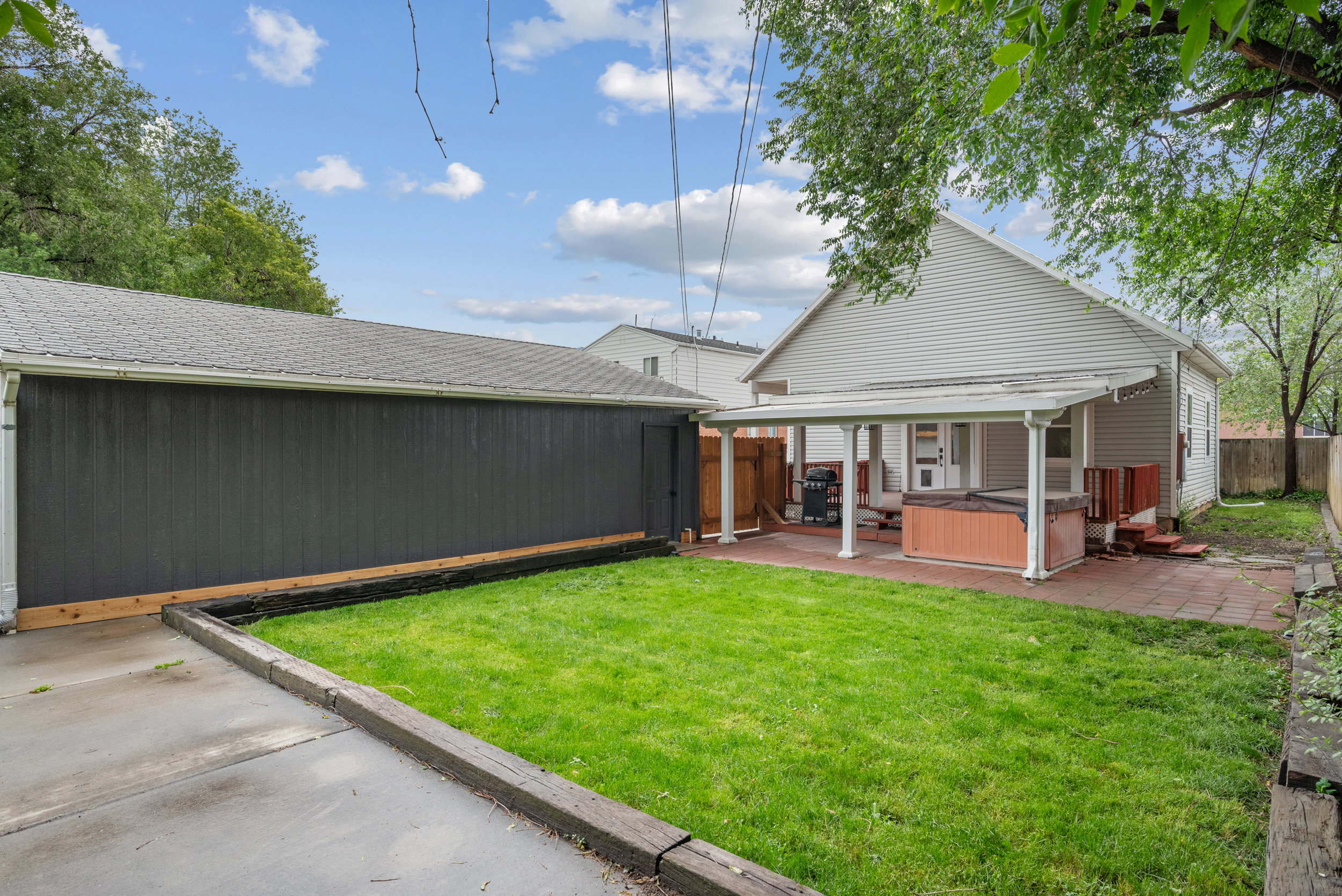 Expansive backyard featuring a manicured lawn, a detached garage with dark siding, and a covered patio with a paved surface