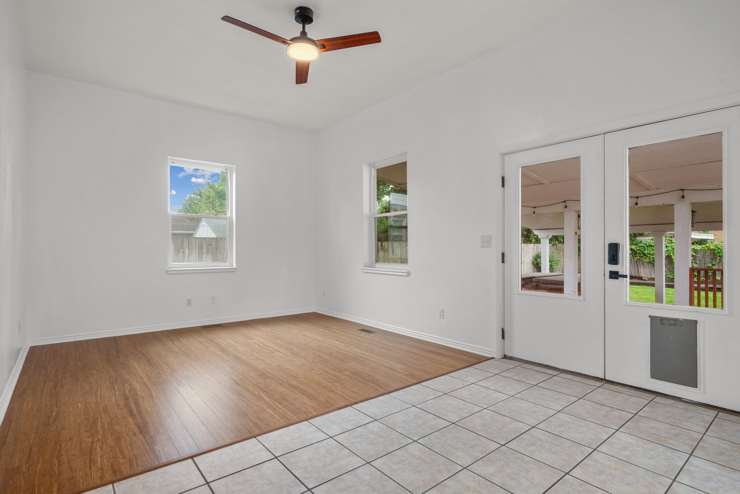 Spacious room featuring wood-finish flooring, a contemporary ceiling fan, and multiple windows