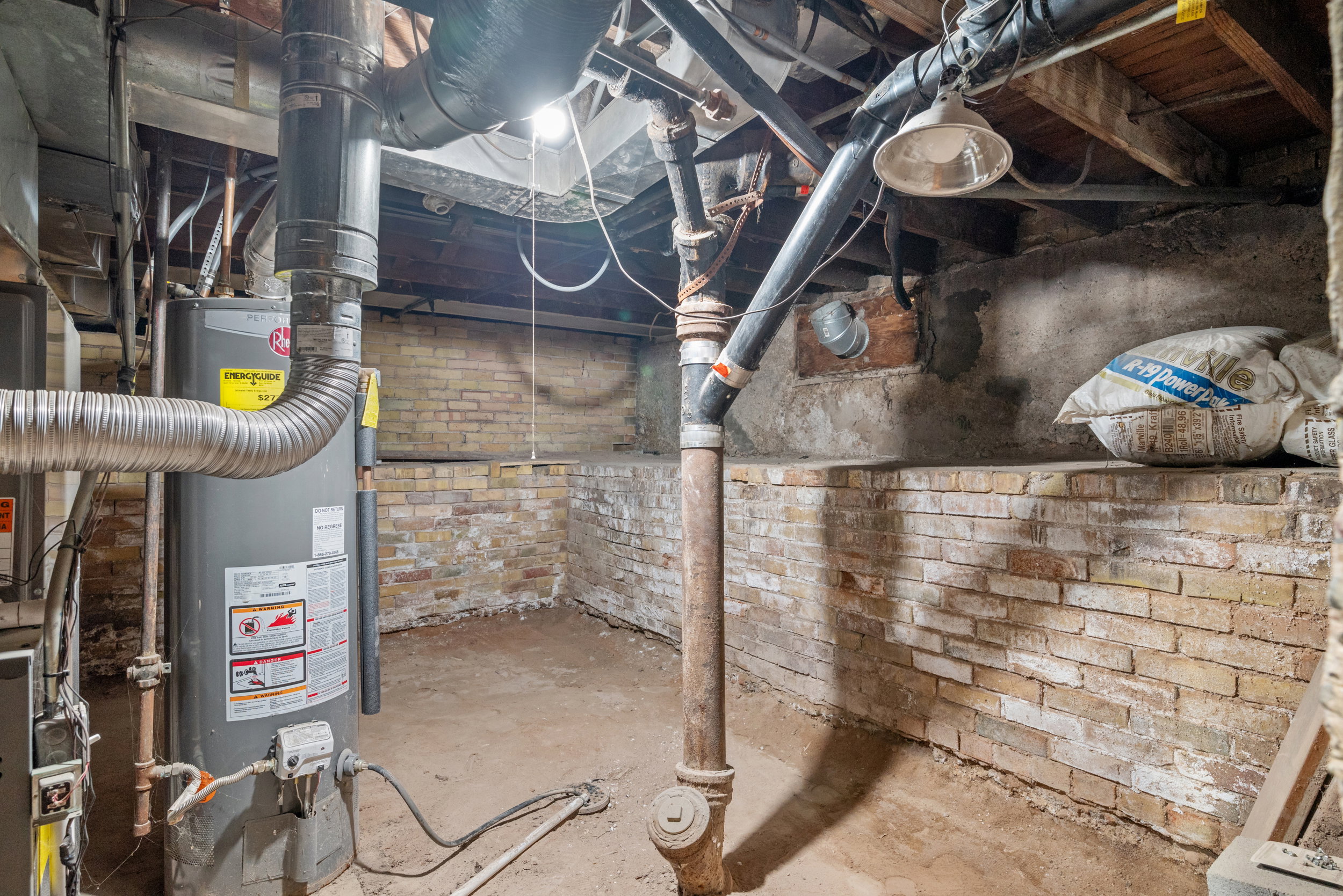 Utility space featuring a water heater, exposed piping, and brick foundation walls