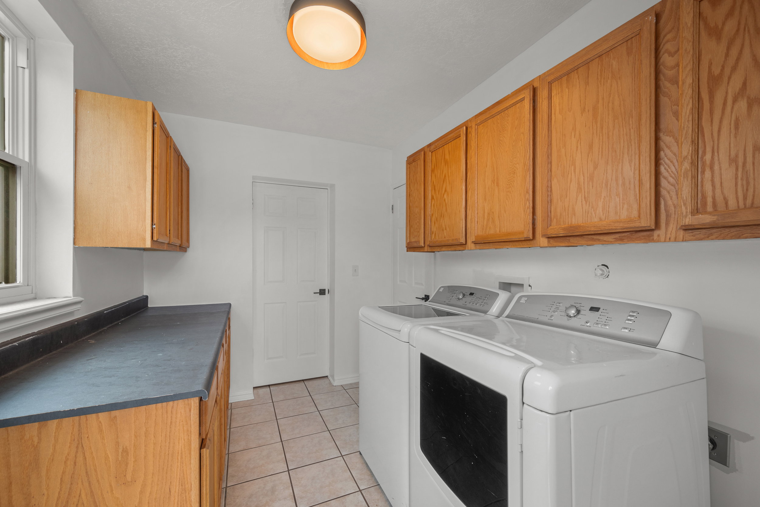 Laundry area featuring wood-finish cabinetry, a dark countertop, and tiled flooring