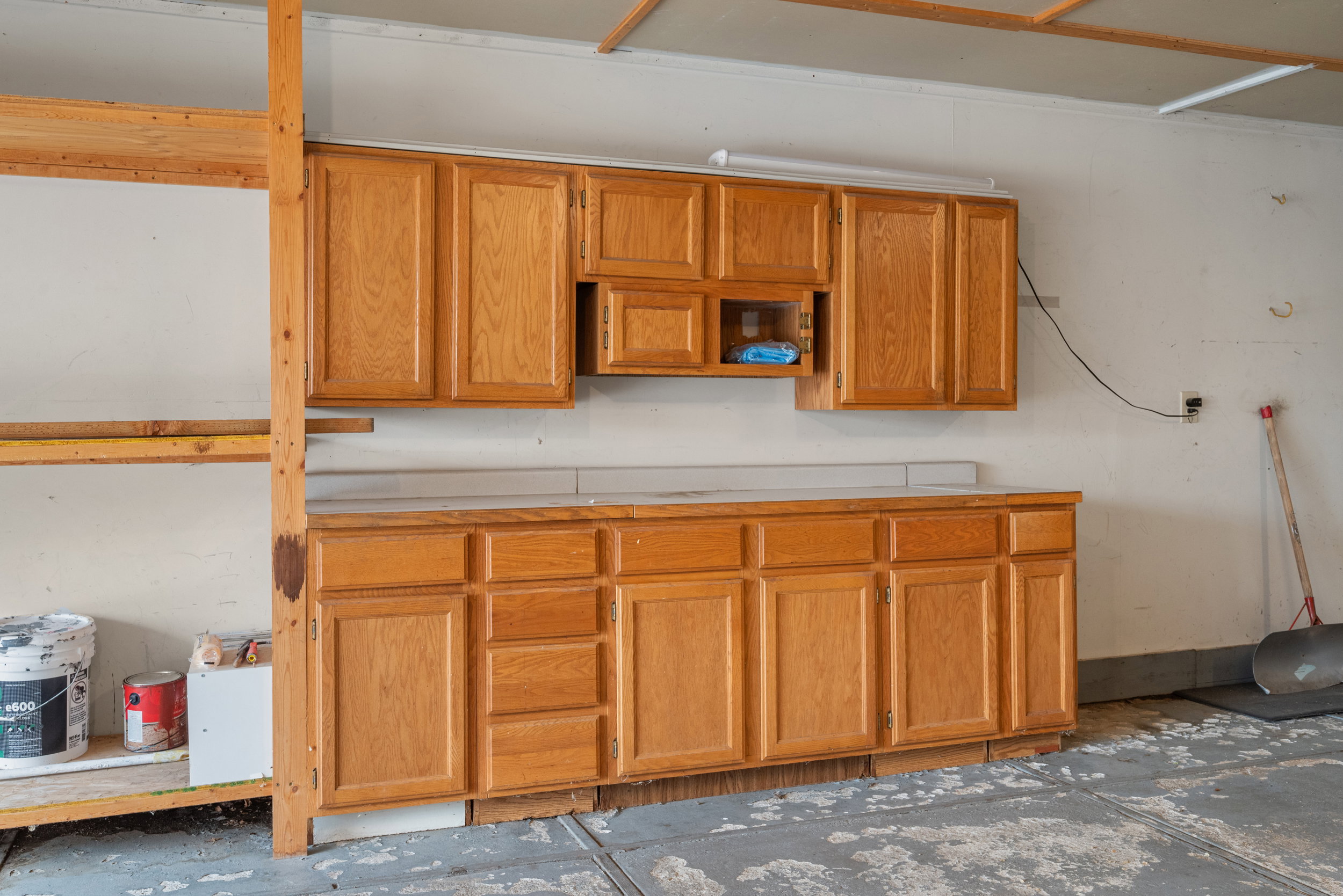 Garage workbench with wood-finish cabinetry, a light-toned countertop, and overhead storage cabinets