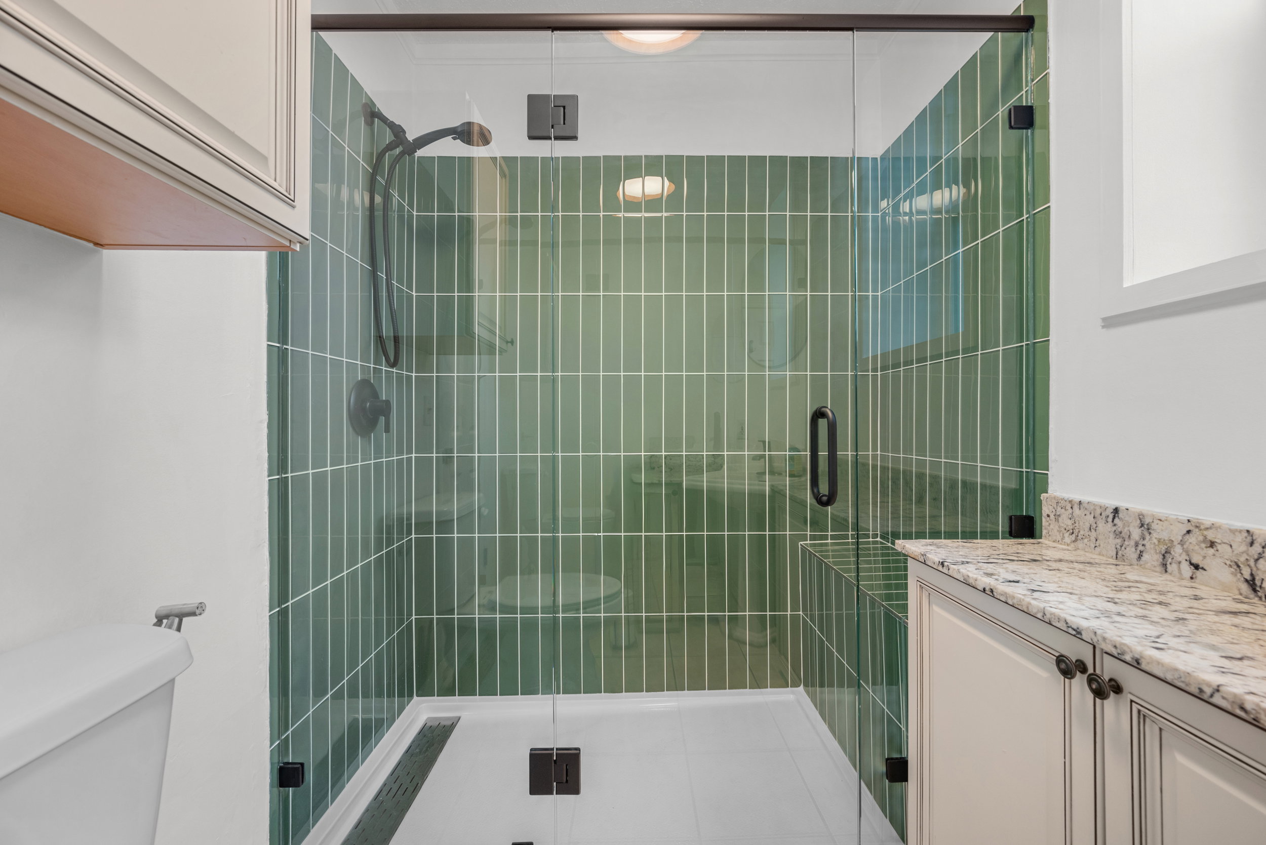 Glass-enclosed shower with vertical green subway tile, integrated shower bench, and dark bronze fixtures