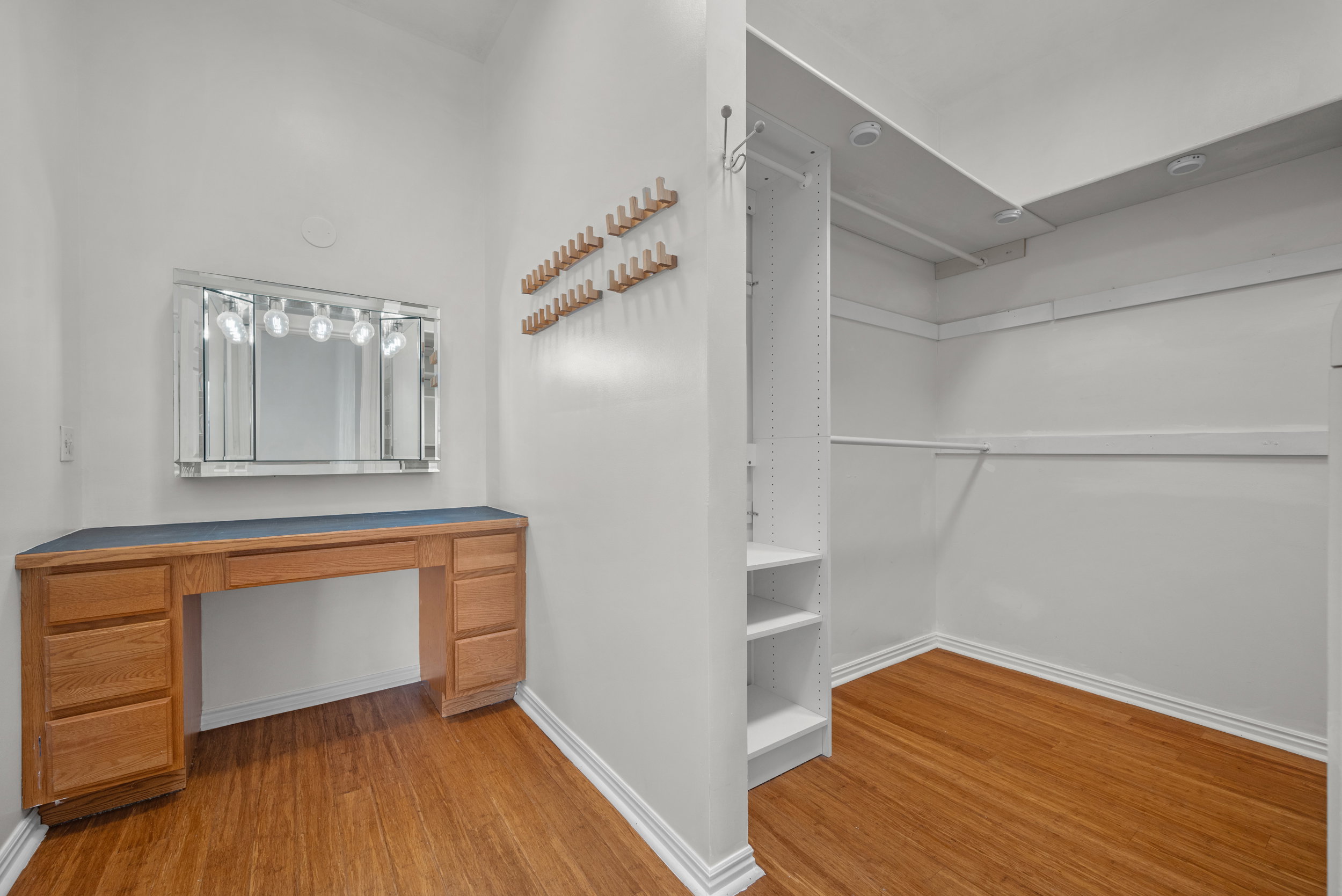 Built-in vanity with integrated lighting, wood-finish flooring, and an adjacent walk-in closet with shelving and hanging rods