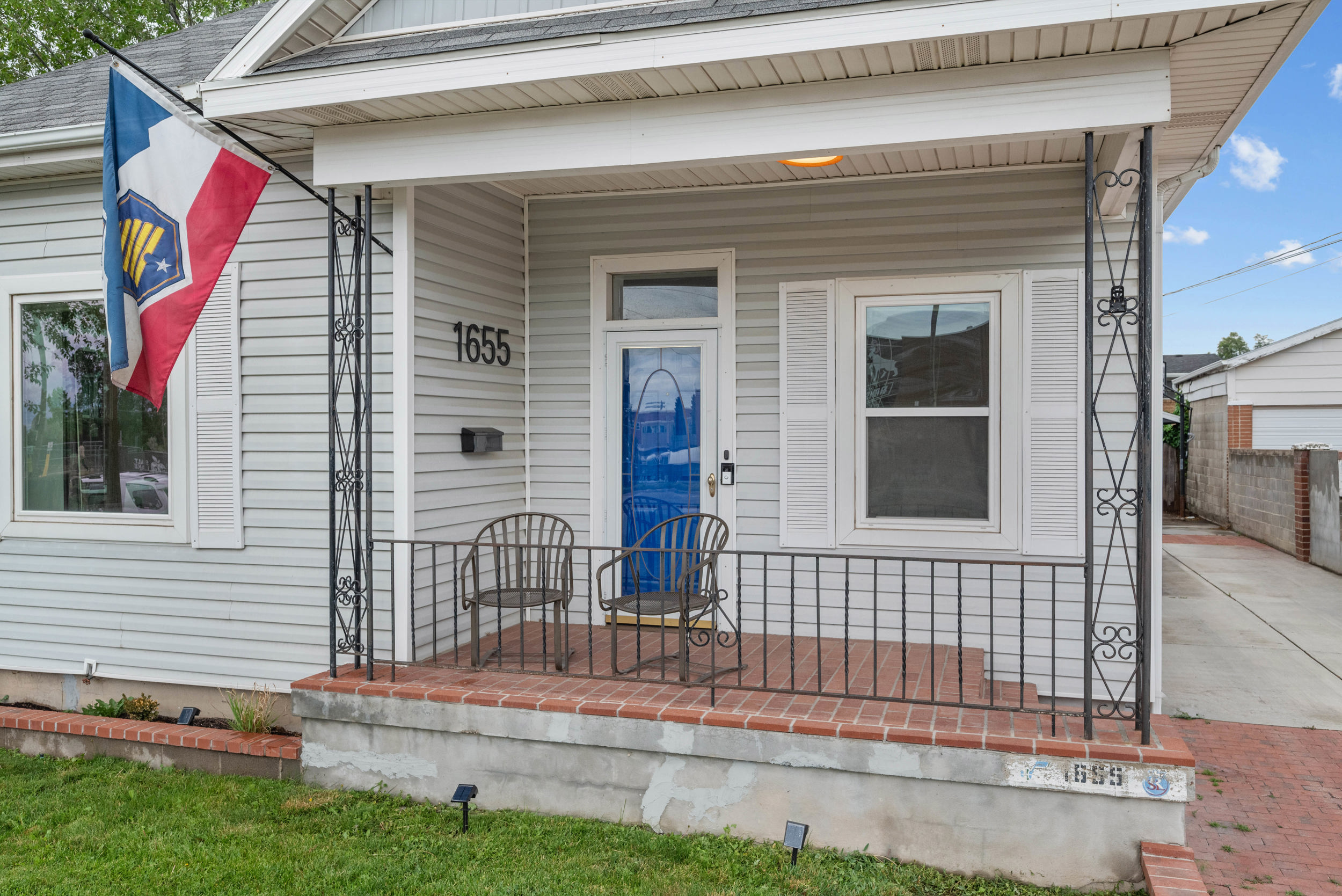 Front porch featuring a red brick-finish floor, black wrought iron railing, and a blue door