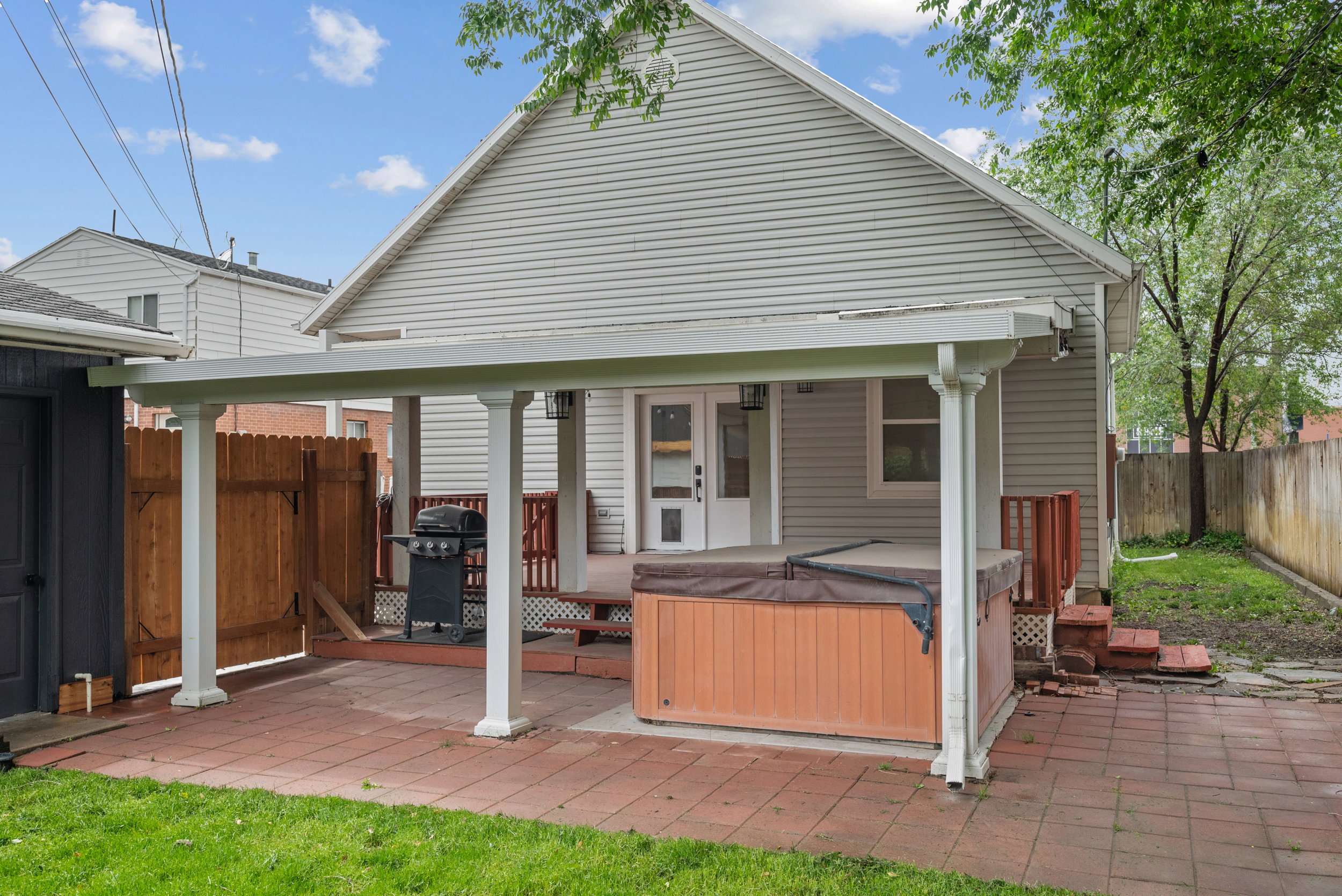 Covered patio featuring red paver flooring and a built-in hot tub