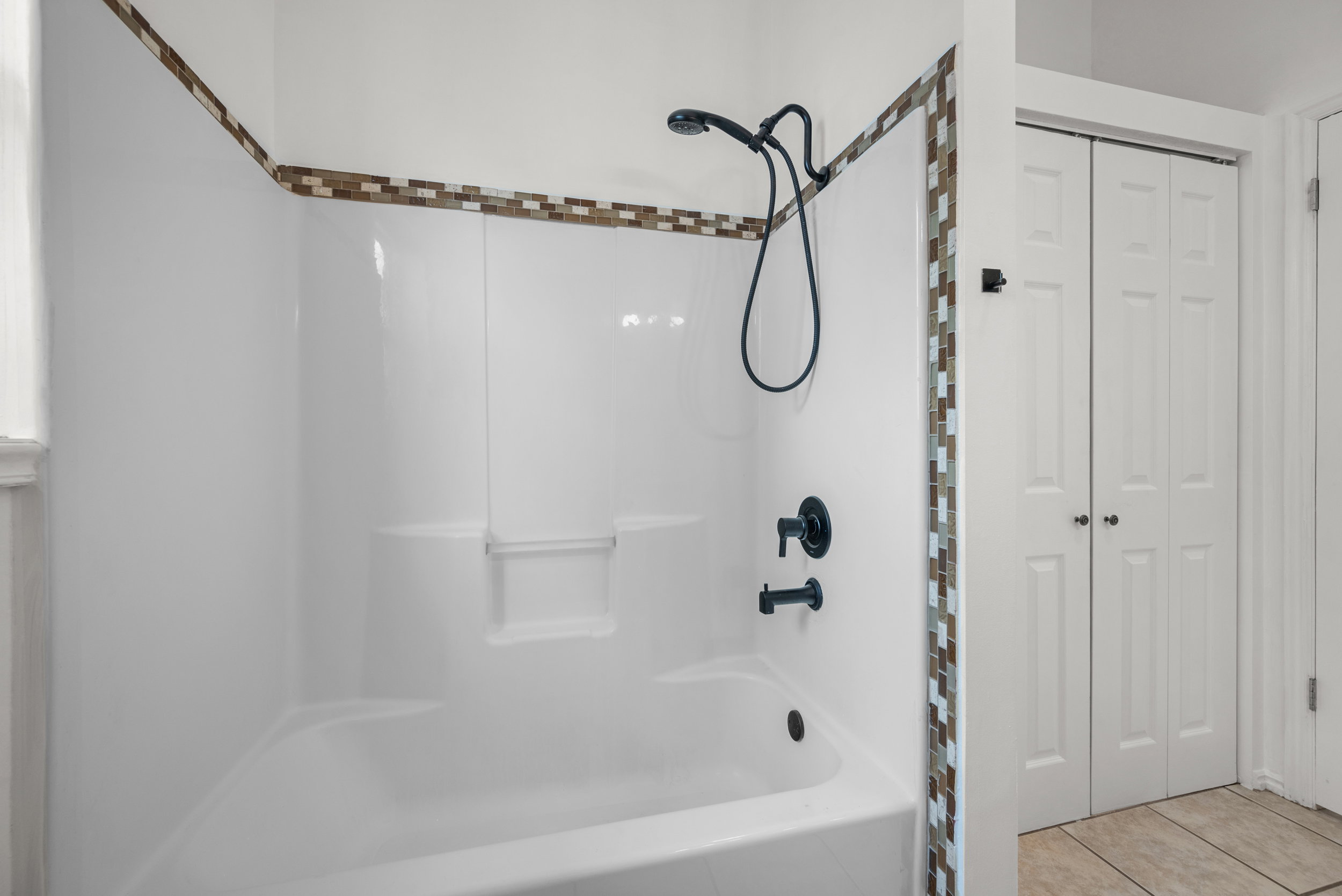 Bathtub/shower combination featuring matte black fixtures and a mosaic tile accent border