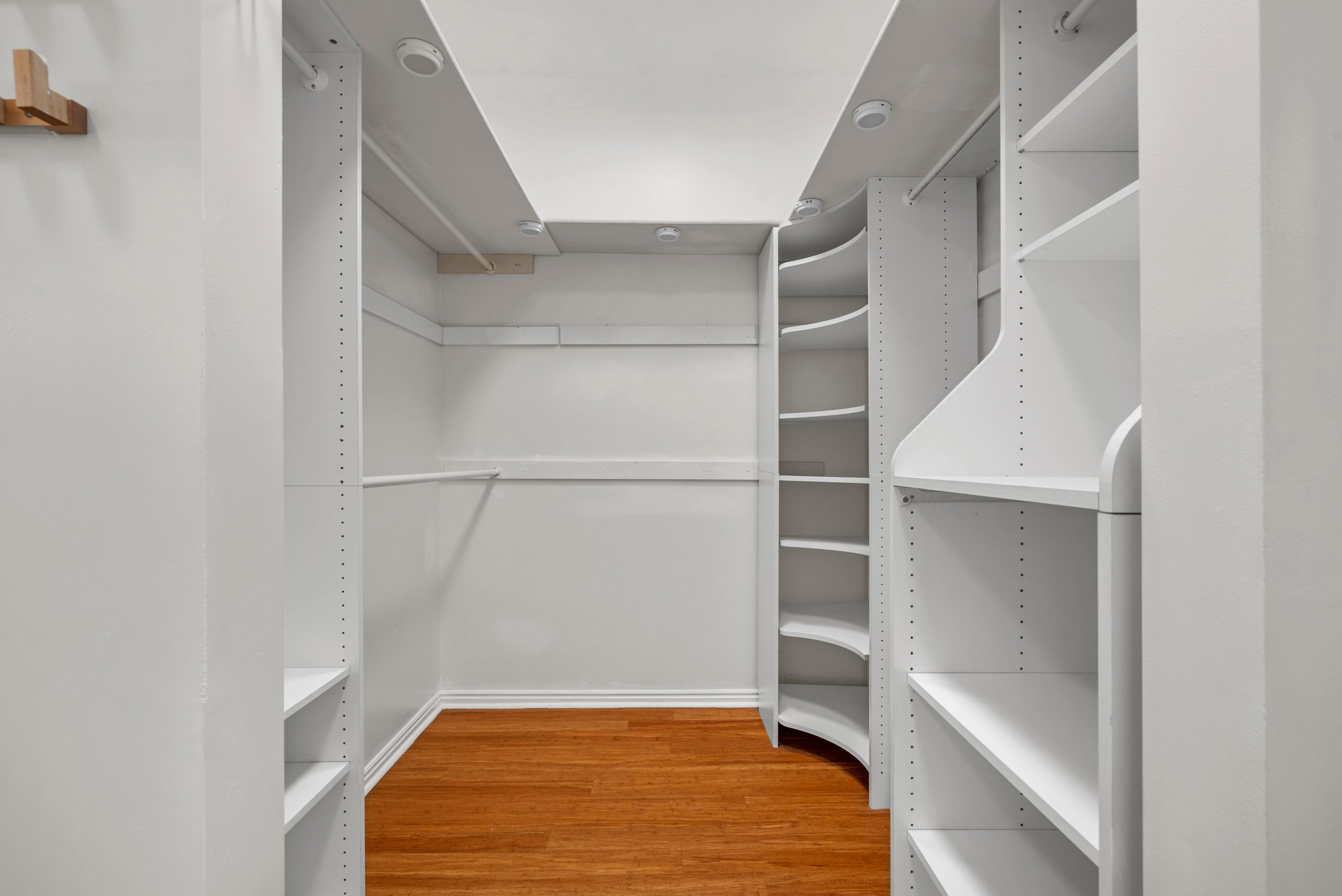 Custom-built closet system featuring adjustable shelving, hanging rods, curved corner shelving, recessed lighting, and wood-finish flooring