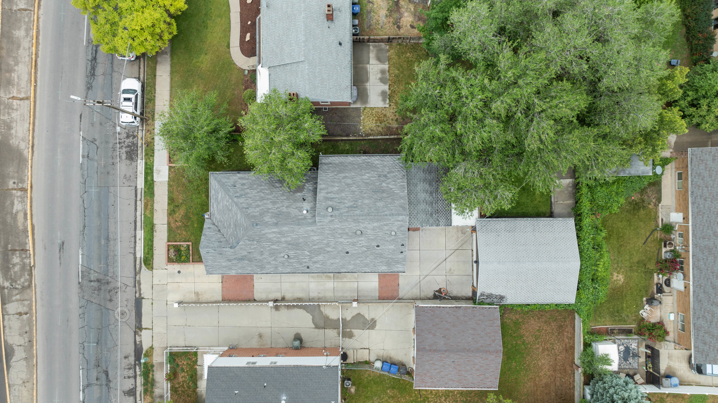 Property with a gray shingle roof, paved driveway, and established trees