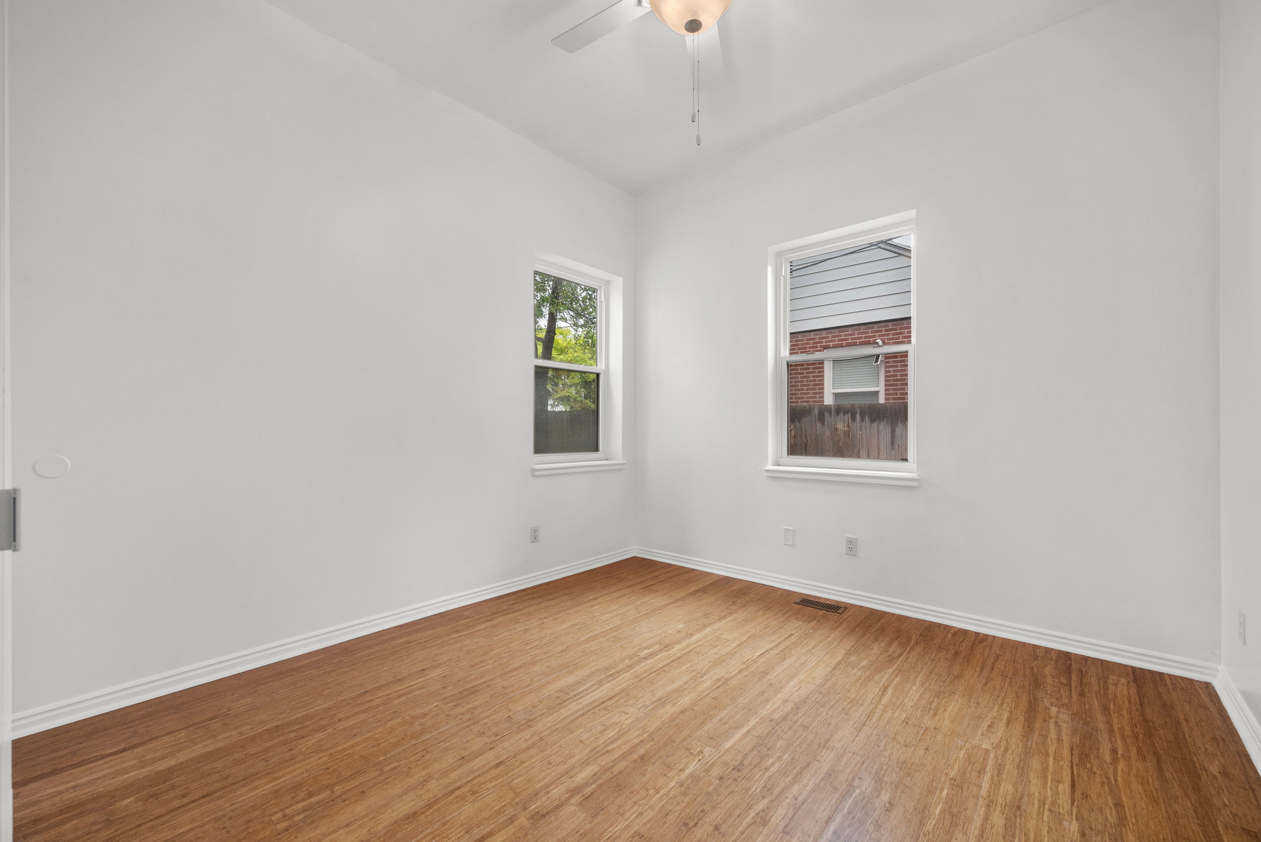 Bright room featuring two windows with white trim, wood-finish flooring, and a ceiling fan with integrated lighting