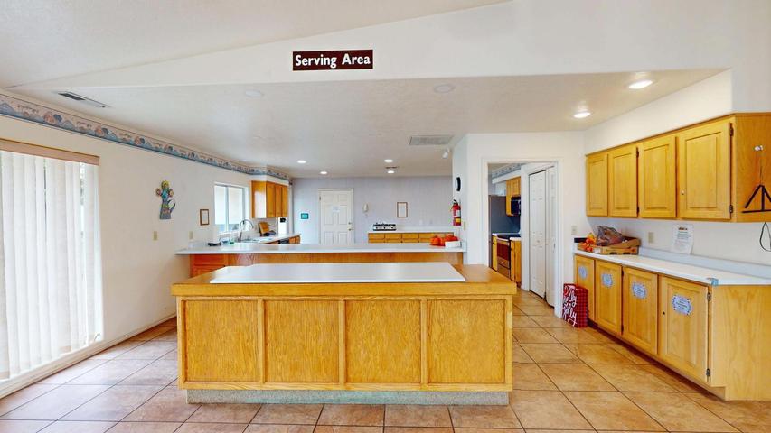 Expansive kitchen featuring an oversized island with a built-in cooktop, extensive cabinetry with wood-finish doors and white countertops, and a full-height glass sliding door