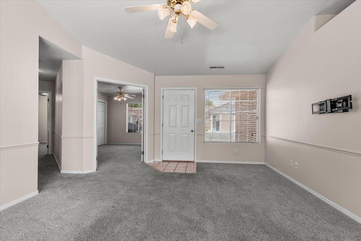 Spacious carpeted room featuring vaulted ceilings, a ceiling fan with light fixture, and a picture window