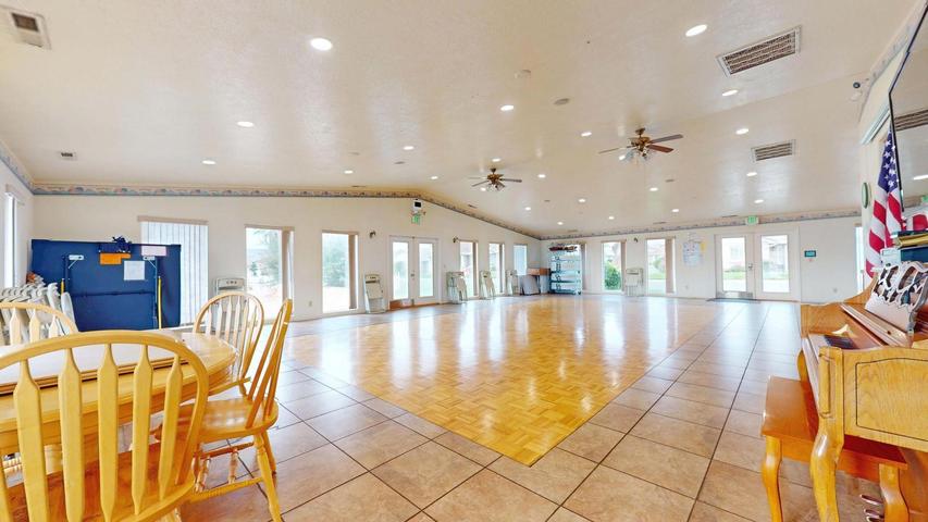 Spacious open room featuring a large wood-finish dance floor, tile flooring, multiple ceiling fans, recessed lighting, and numerous glass-paned doors providing abundant natural light