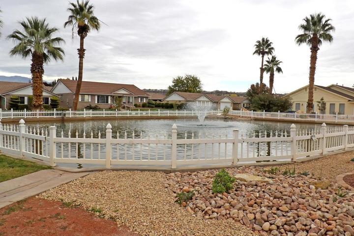 Fenced pond featuring a central fountain, surrounded by mature palm trees, residential homes, and a xeriscaped foreground with various rock sizes