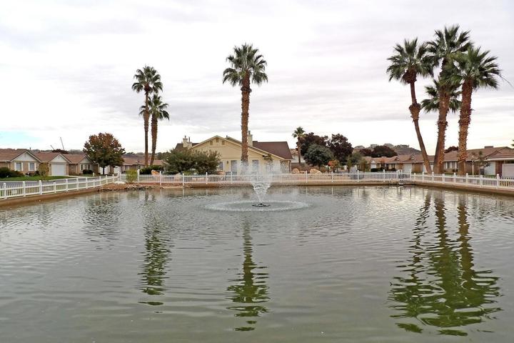 Lush pond featuring a central fountain, surrounded by a white picket fence
