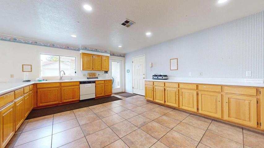 Spacious kitchen featuring extensive wood cabinetry, light countertops, a built-in dishwasher, and a large window above the sink