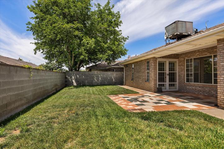Expansive backyard featuring a patterned paver patio, brick exterior, double glass doors, and a concrete block perimeter wall