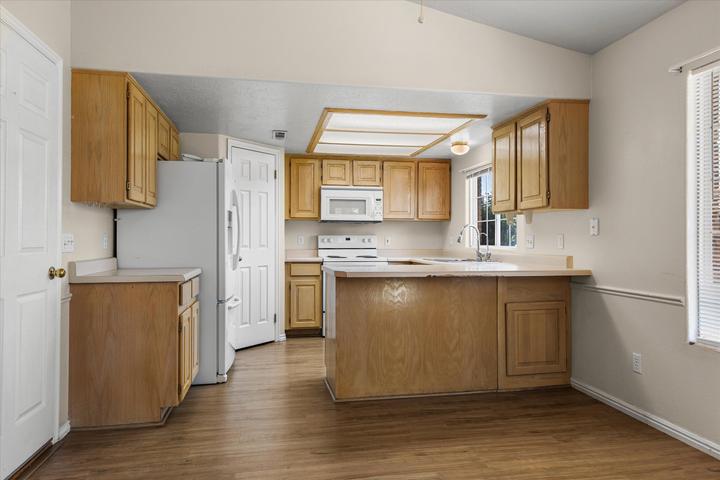 Kitchen featuring wood-finish cabinetry, white appliances, and a vaulted ceiling
