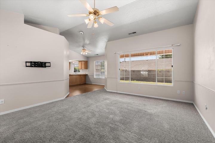 Spacious living area featuring vaulted ceilings with ceiling fans, a large picture window, and neutral gray carpeting