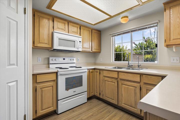 Kitchen featuring wood-finish cabinetry, light countertops, and a white electric range with an overhead microwave