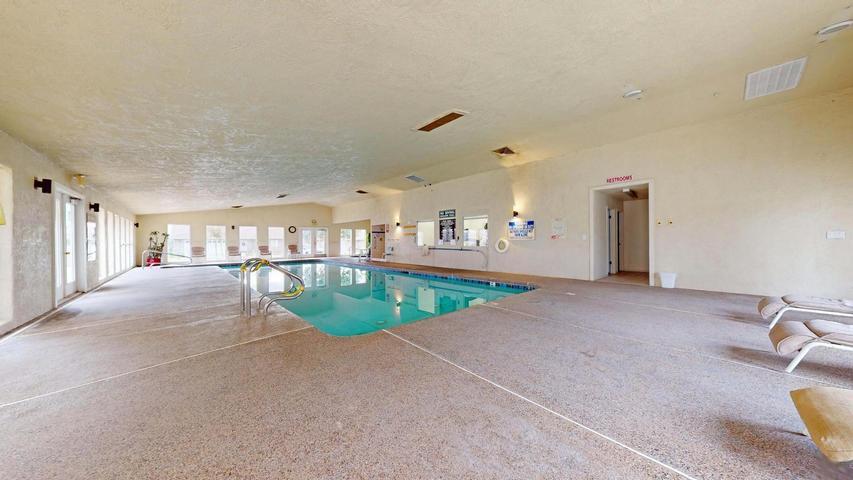 Indoor swimming pool featuring an integrated entry ladder, light-colored textured flooring, and multiple window-paned doors