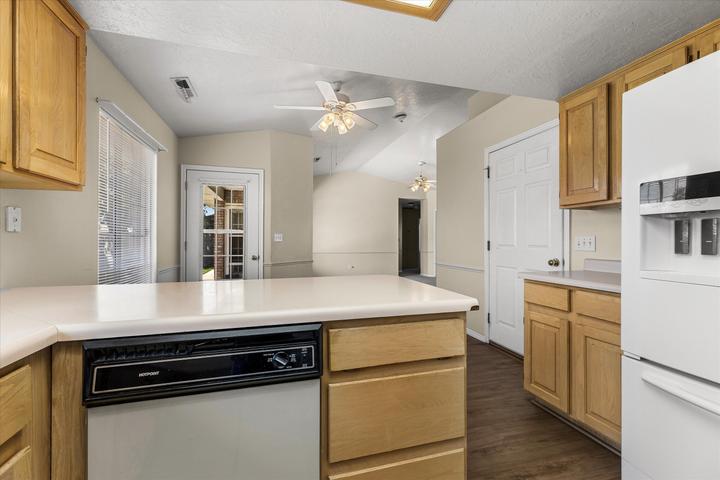 Kitchen featuring wood-finish flooring, light wood cabinetry, a breakfast bar with solid surface countertops, and an integrated dishwasher