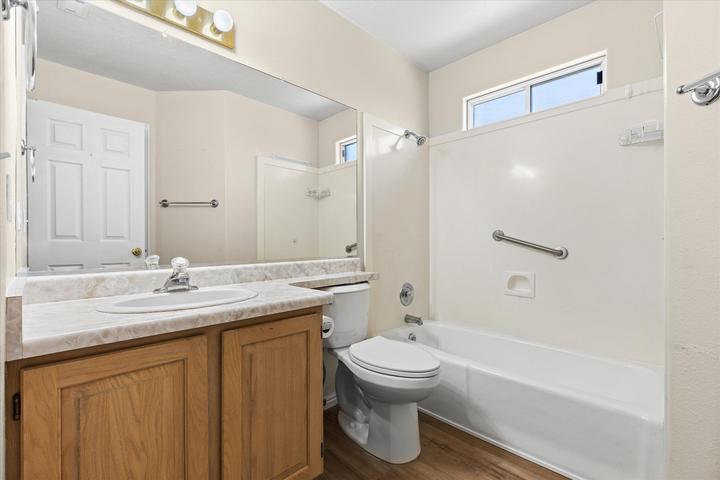 Bathroom featuring a single vanity with wood-finish cabinetry, a large wall-mounted mirror, a tub/shower combination with grab bars, and a privacy window