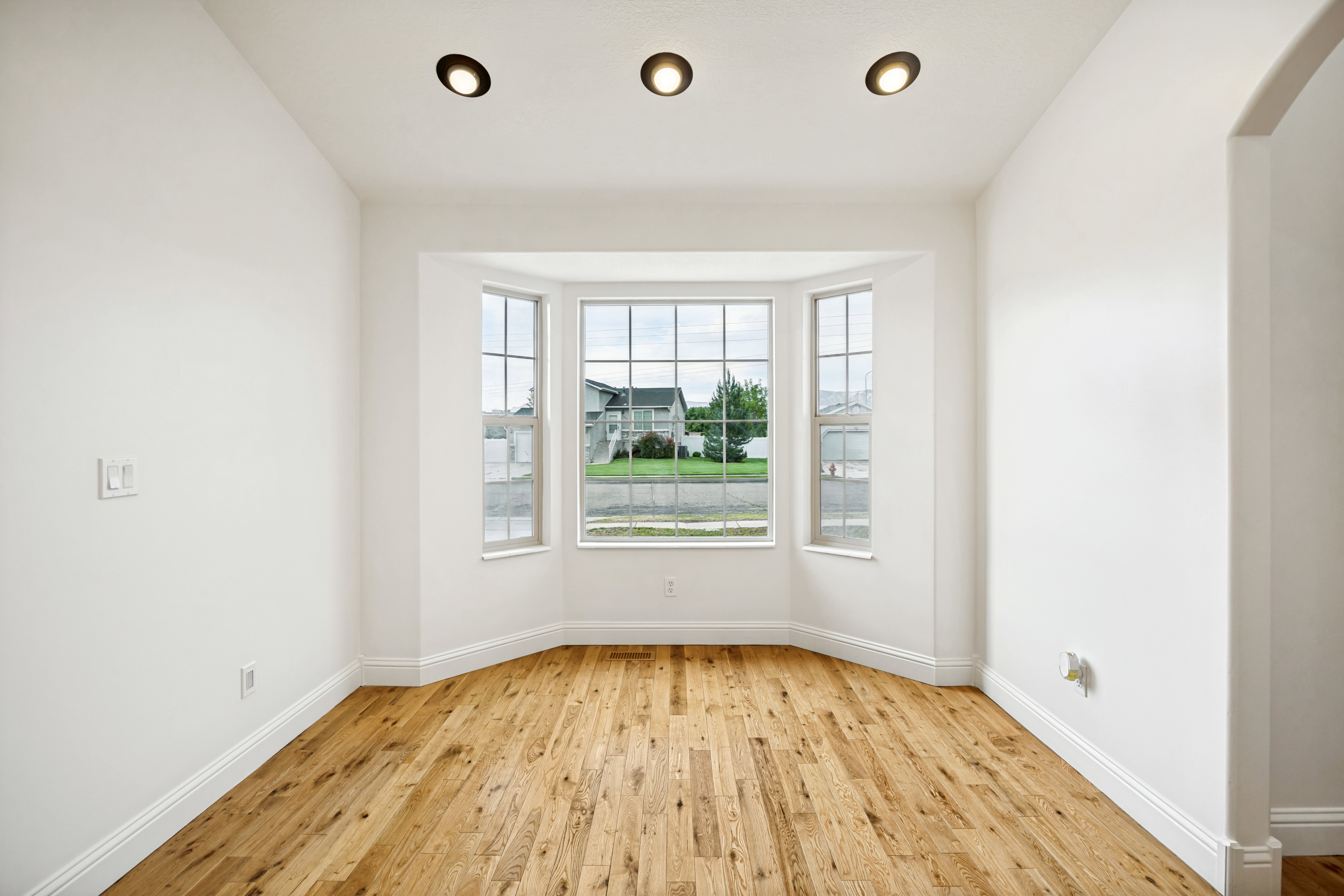 Bay window with multiple panes, hardwood flooring, recessed lighting, white trim, and a curved archway