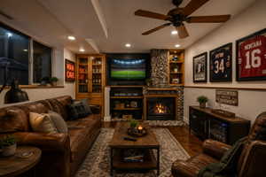 Cozy living area featuring a stone-clad fireplace with wood mantle, built-in shelving, recessed ceiling lighting, and wood-finish flooring