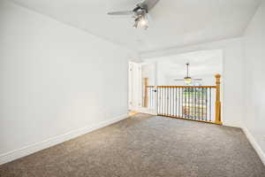 Carpeted room with white walls, a ceiling fan with track lighting, and a doorway opening to a railing with decorative metal spindles