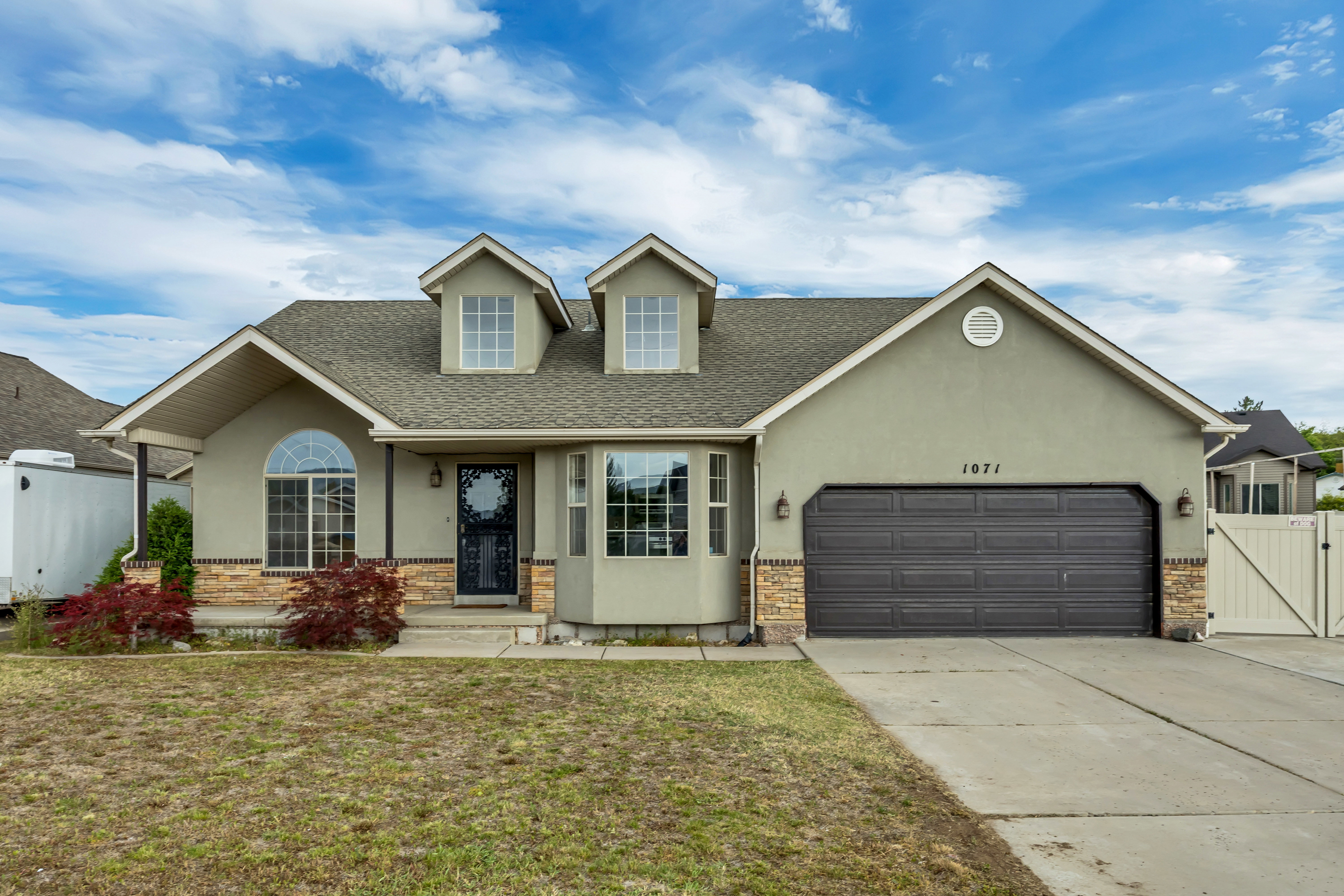 Stucco exterior featuring a two-car garage, dormer windows, and a covered entry