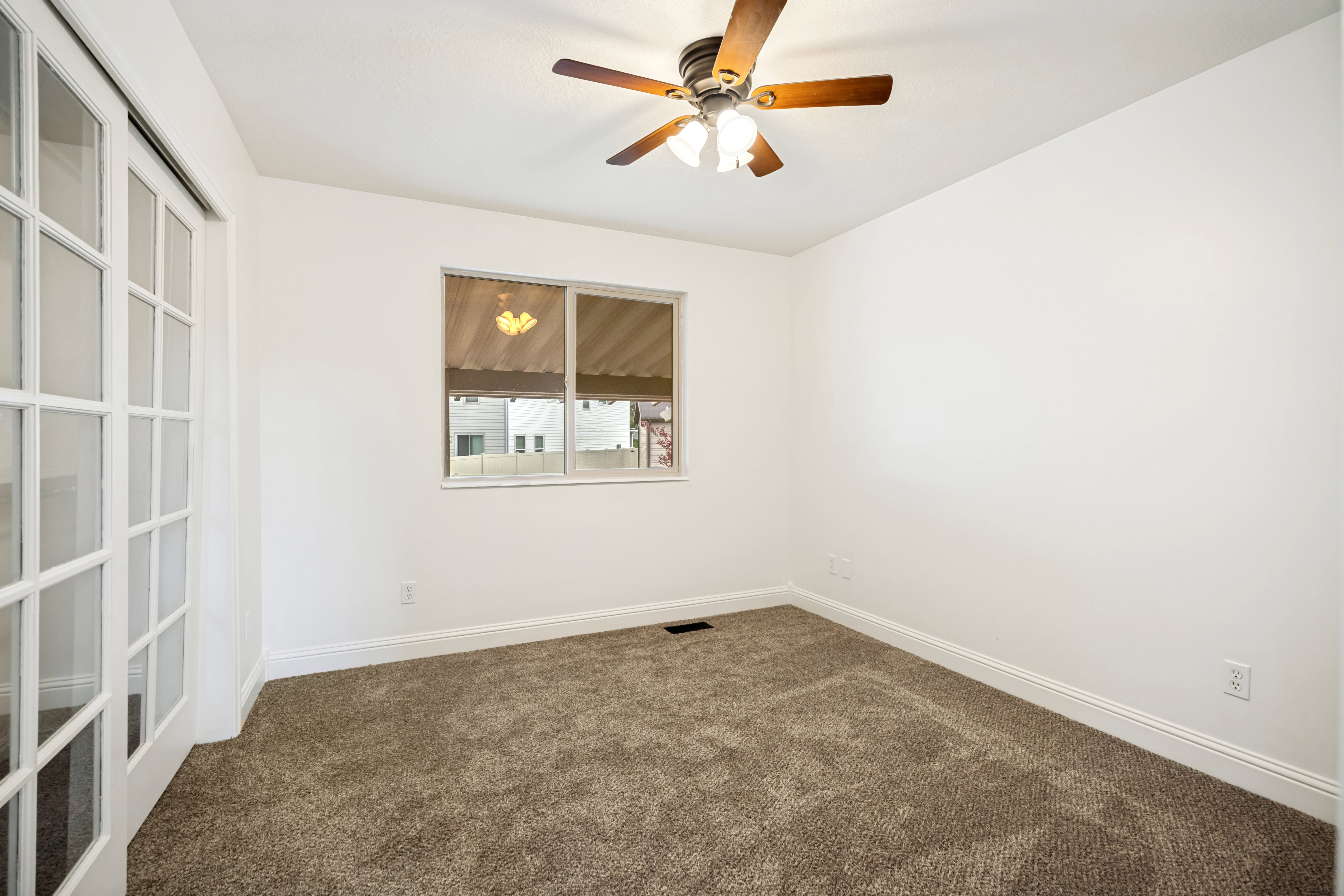 Spacious room featuring white walls, brown carpet, a window, and a ceiling fan with integrated lighting