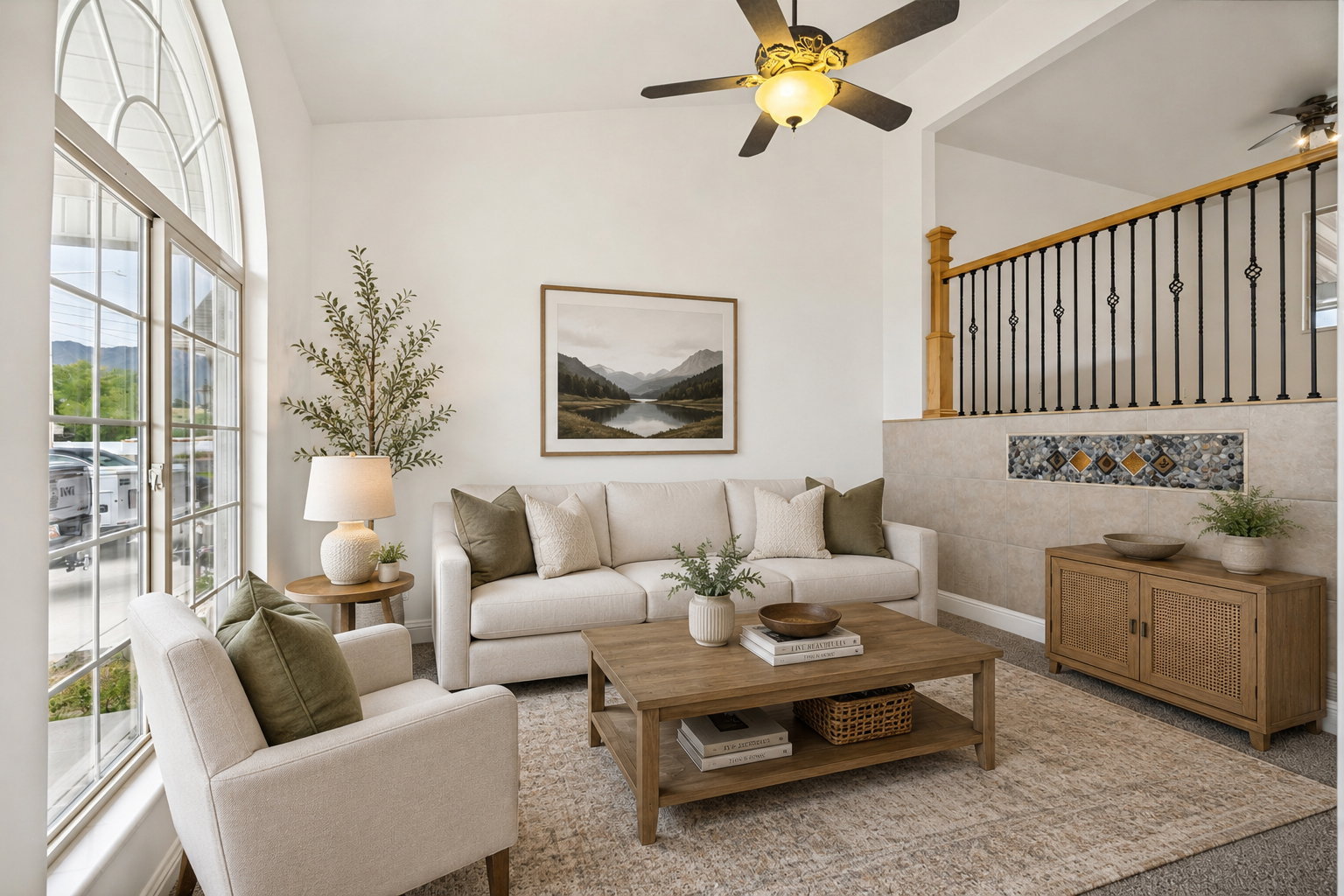 Spacious living area featuring a large arched window, ceiling fan, and staircase with wooden handrail and wrought iron balusters