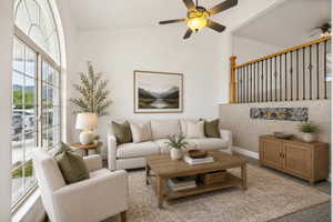 Spacious living area featuring a large arched window, ceiling fan, and staircase with wooden handrail and wrought iron balusters
