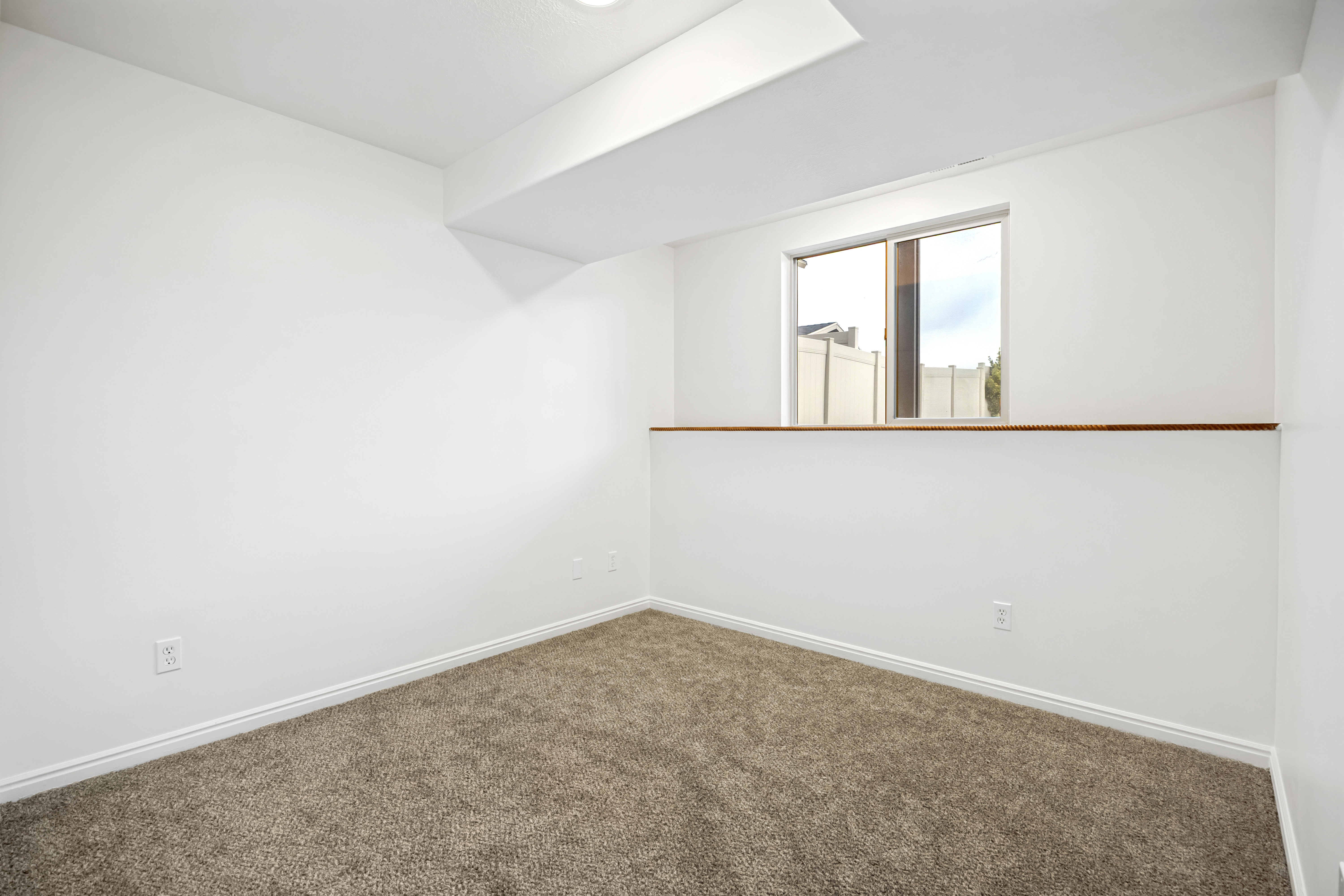Carpeted room featuring a white interior, egress window, white baseboards, and ceiling-mounted lighting