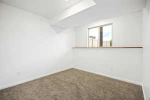 Carpeted room featuring a white interior, egress window, white baseboards, and ceiling-mounted lighting