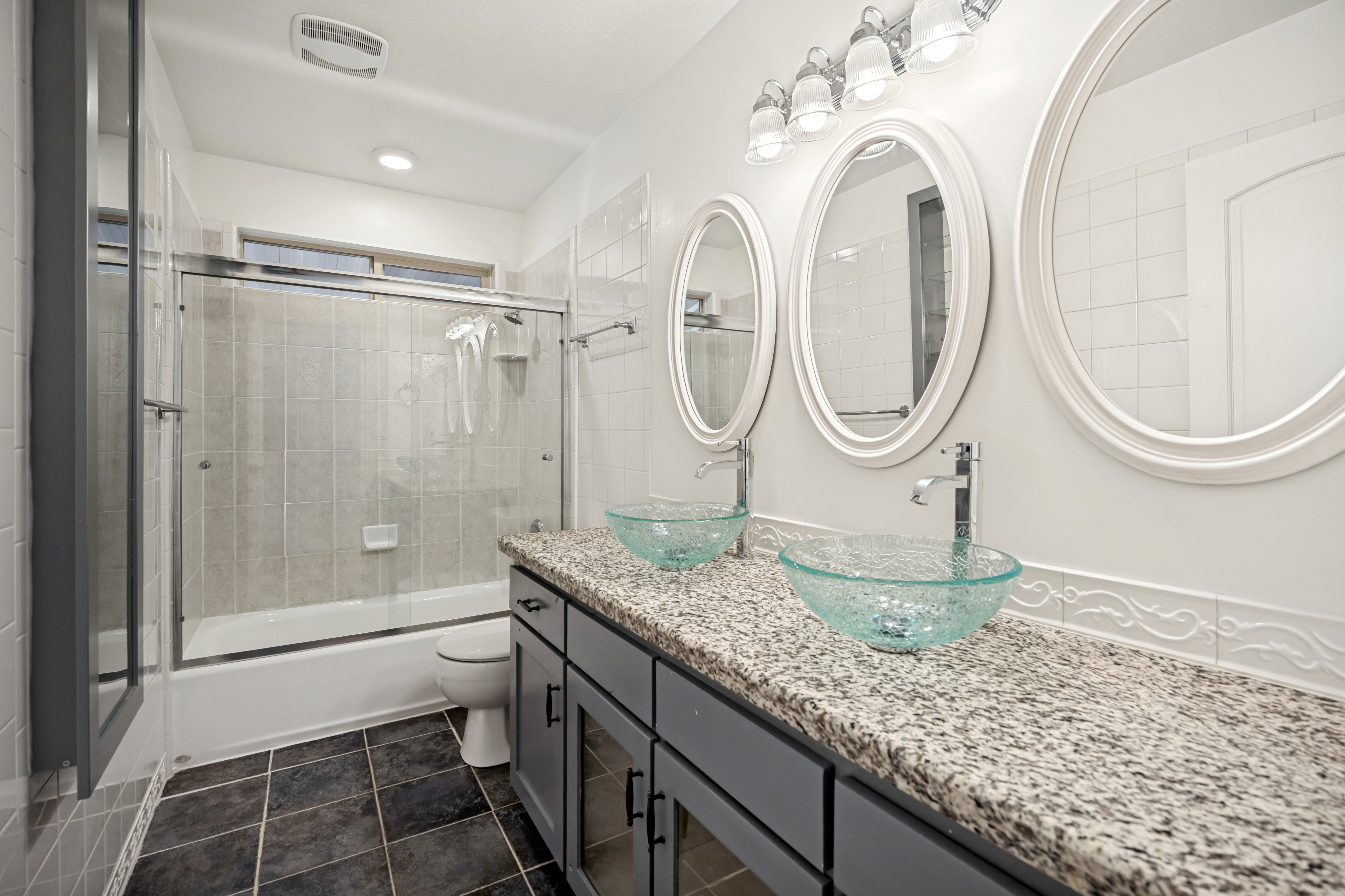 Dual vessel sinks set atop a granite-style countertop and gray cabinetry
