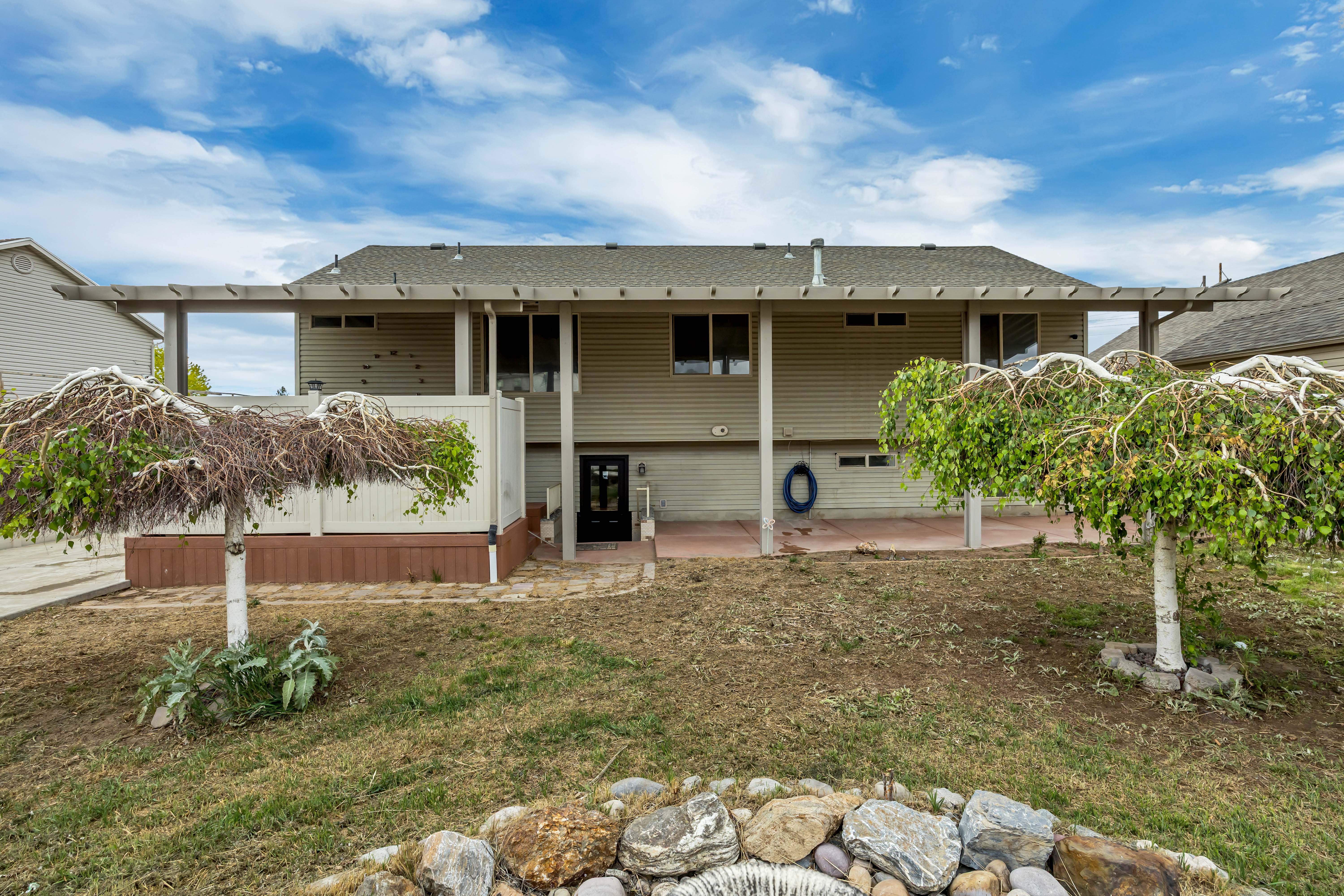 Rear exterior with a full-width covered patio, featuring a lattice pergola and concrete flooring