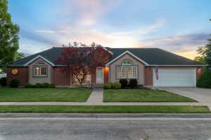 Brick and stucco exterior featuring a two-car garage, mature landscaping, and an arched window