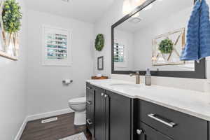 Bathroom featuring dark wood-finish flooring, white walls, and a window with white plantation shutters